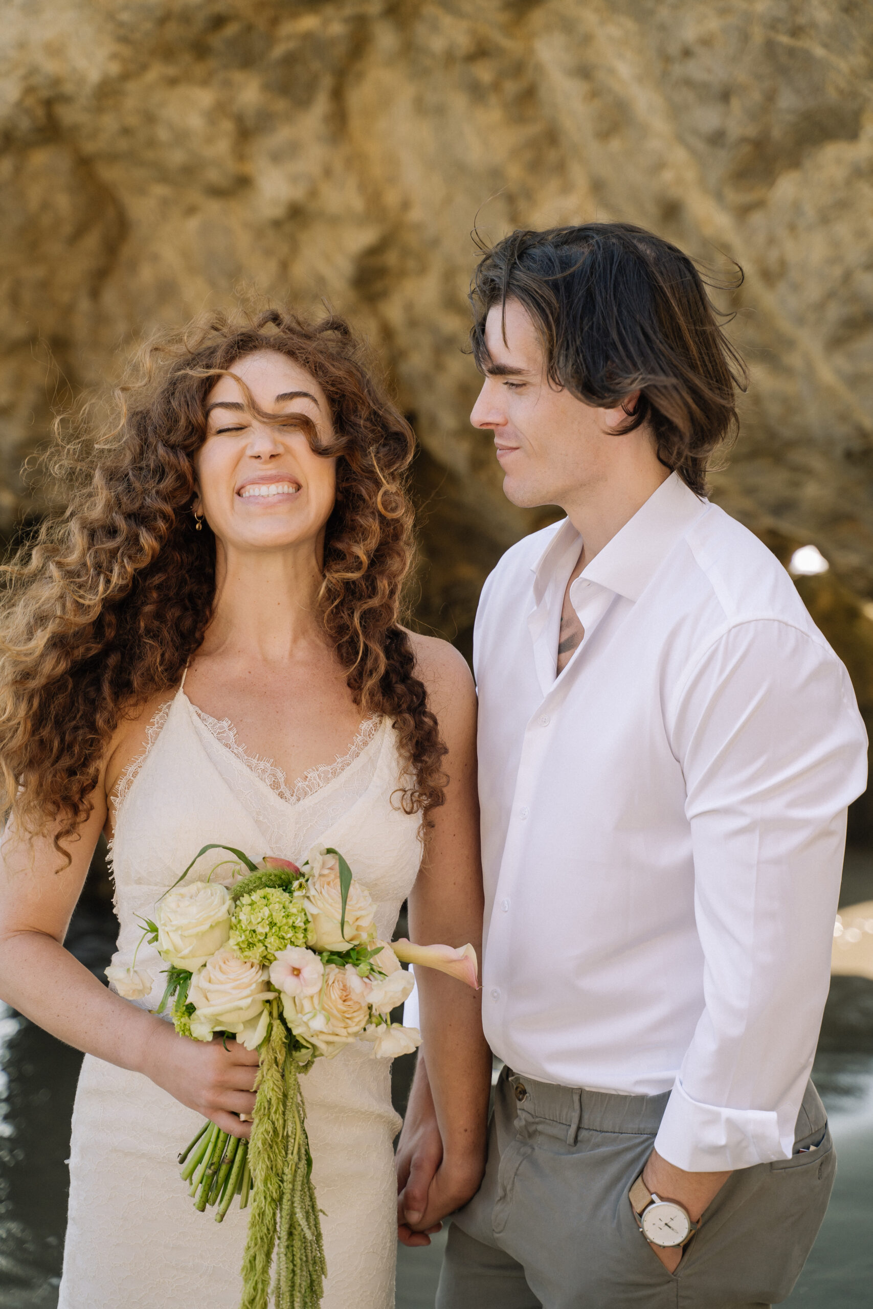 Bride smiles as groom looks at her on El Matador Beach during elopement.